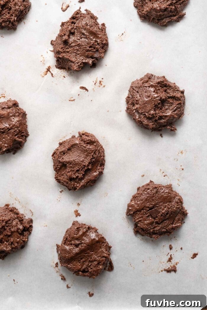 Irresistible Vegan Chocolate Peppermint Delights 6 Unbaked, flattened vegan chocolate cookies arranged on a parchment-lined baking tray.