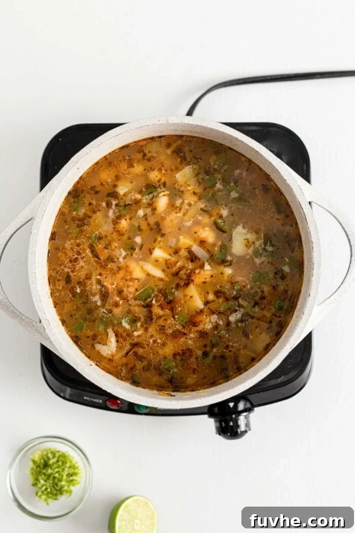 Creamy Vegan White Bean Chili 7 Soup with beans and potato cooking in a large pot on a small induction cook top, rich and bubbling.