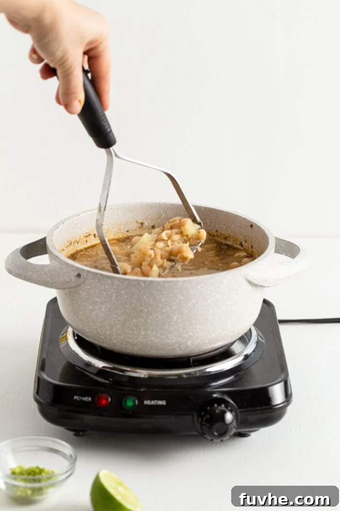 Creamy Vegan White Bean Chili 8 Mashing a pot of potato and beans with a potato masher in a pot, creating a creamy texture.