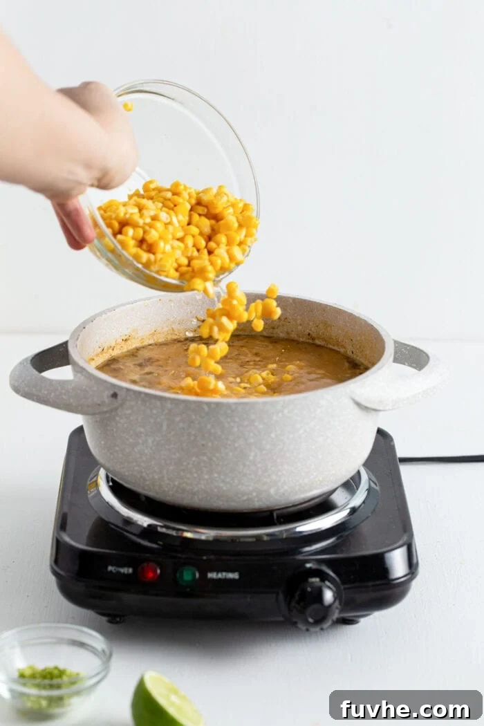 Creamy Vegan White Bean Chili 9 Adding a bowl of corn to chili cooking in a large pot, vibrant and fresh.