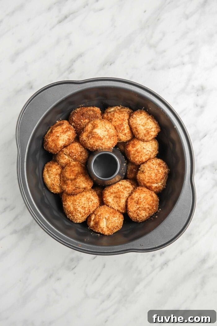 Raw, coated vegan monkey bread dough balls arranged in layers within a greased bundt pan, ready for the second rise.