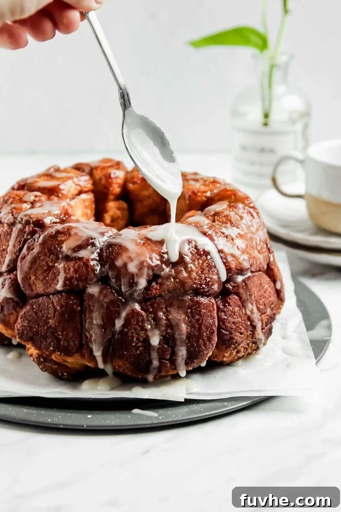 A spoon elegantly drizzling white icing over a freshly baked vegan monkey pull-apart bread on a serving plate, creating a tempting finish.