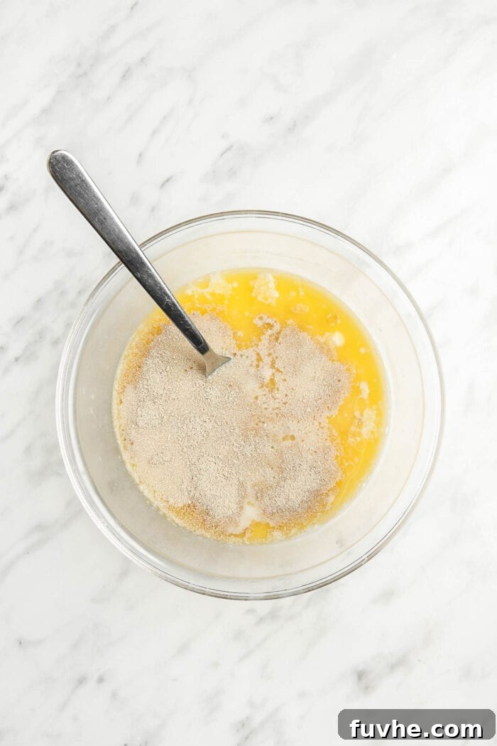 Yeast, warm milk, sugar, and melted vegan butter mixed together in a small, glass mixing bowl, activating the yeast.