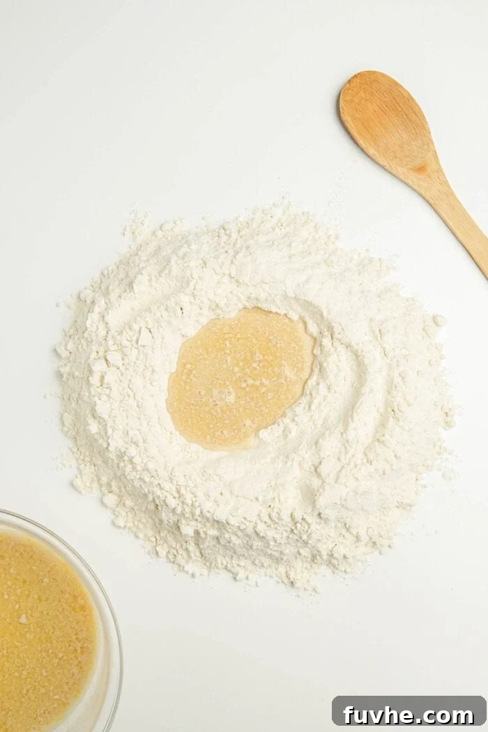 A pile of sifted flour with a well of liquid in the middle, ready for mixing, on a marble surface.
