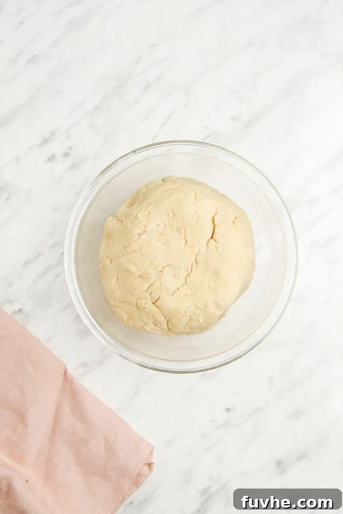 A perfectly smooth, rounded ball of vegan bread dough resting in a glass mixing bowl, covered for rising.