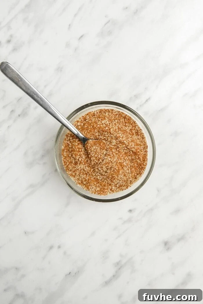 Cinnamon, brown sugar, and cane sugar mixed together in a small glass bowl with a spoon, forming the sweet coating.
