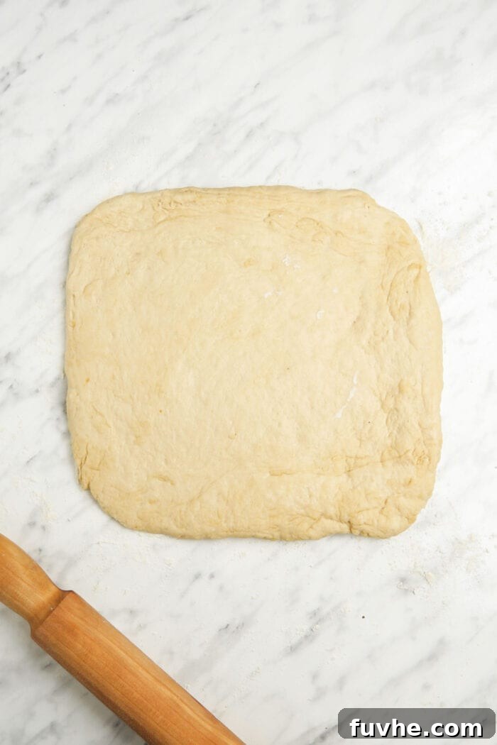 Proofed bread dough rolled out into an 8-inch square on a lightly floured marble surface, ready for cutting.
