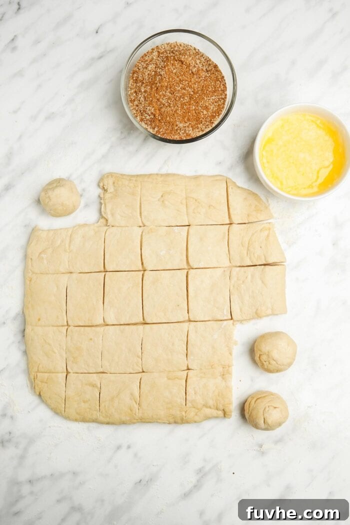 Bread dough rolled out and meticulously cut into 1-inch square pieces on a marble surface, ready to be shaped into balls.