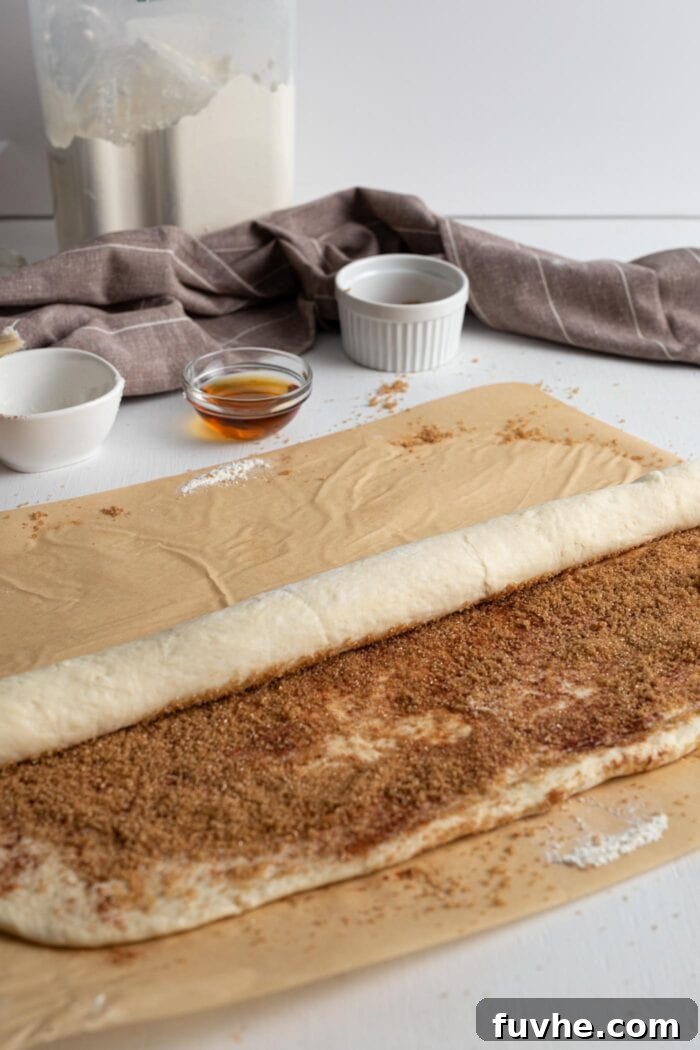 Cinnamon roll dough being meticulously rolled into a tight, even log from one end to the other.