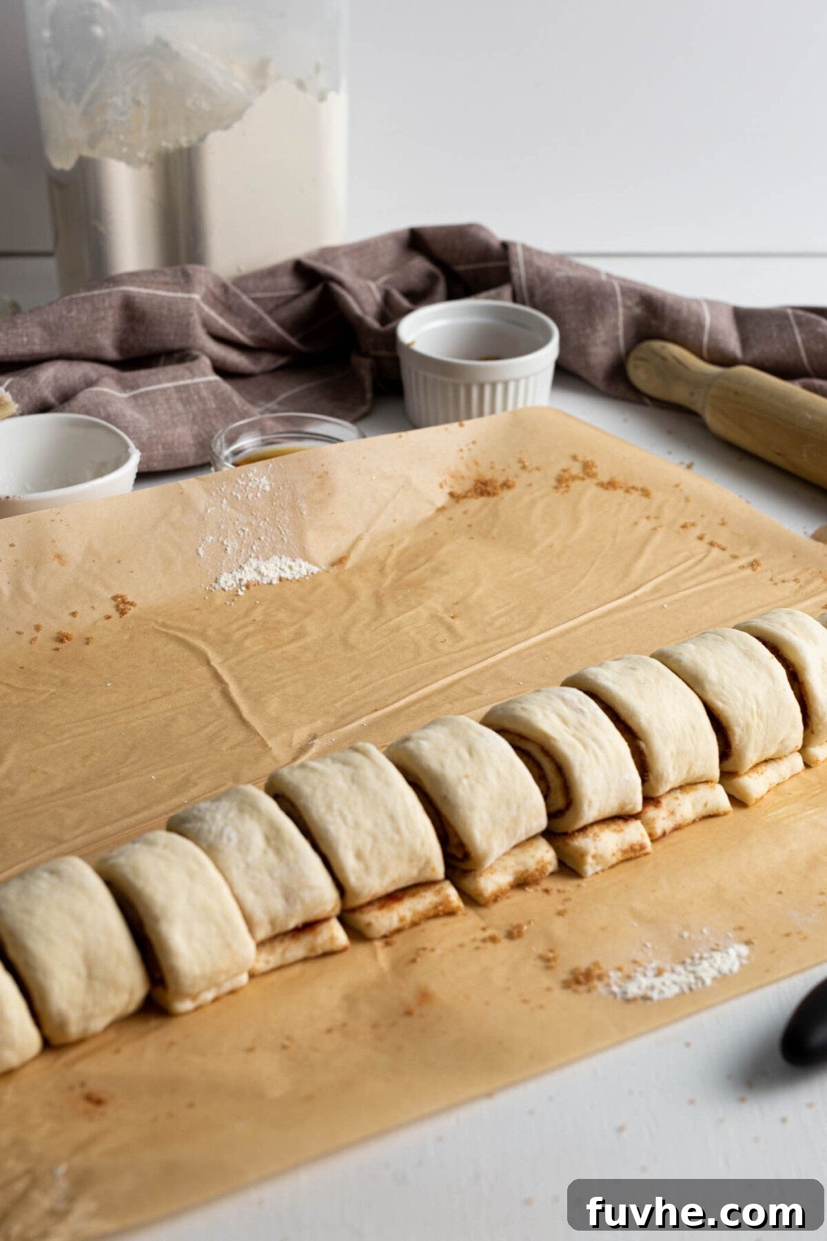 Raw cinnamon roll dough neatly sliced into 12 individual portions, showcasing the cinnamon swirl.