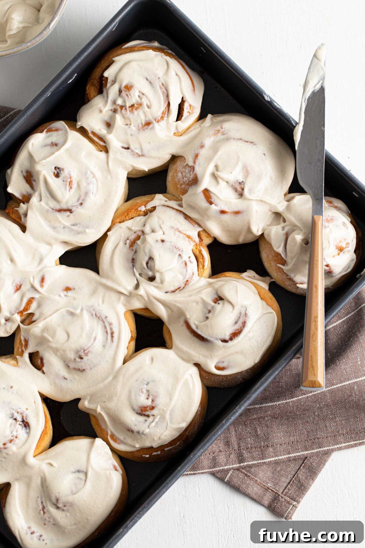 Overhead view of an entire pan of baked vegan cinnamon rolls, generously topped with creamy white icing.