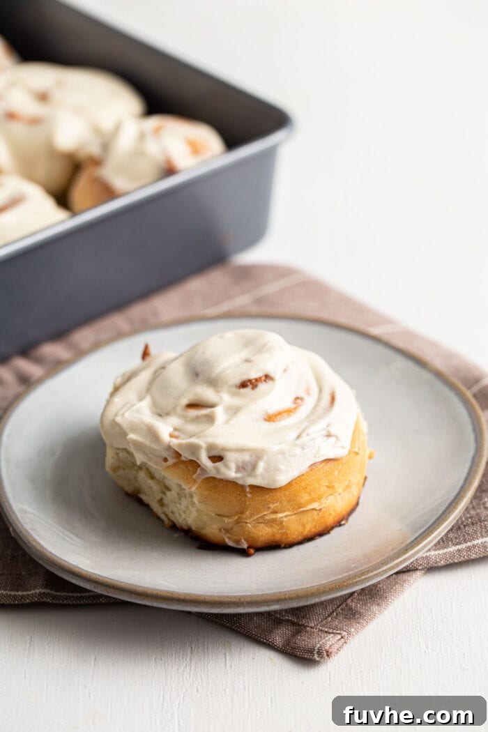 A single, perfectly iced vegan cinnamon bun resting on a small, elegant white plate.