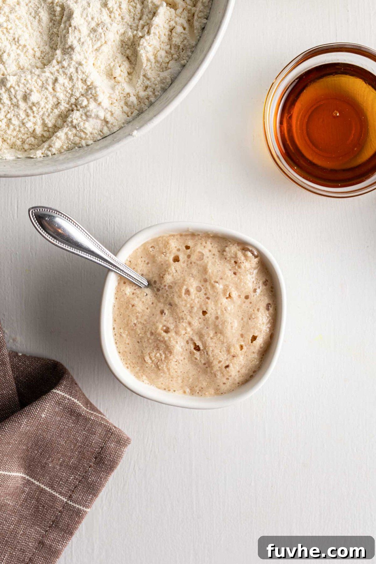 Close-up of a small bowl containing frothy, activated yeast mixture with a spoon resting inside.