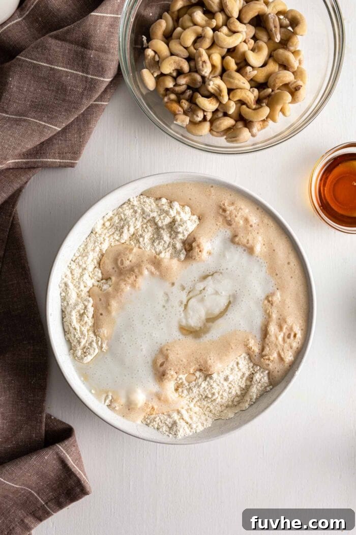 A mixing bowl showing wet and dry ingredients for vegan cinnamon rolls partially combined, forming a shaggy dough.