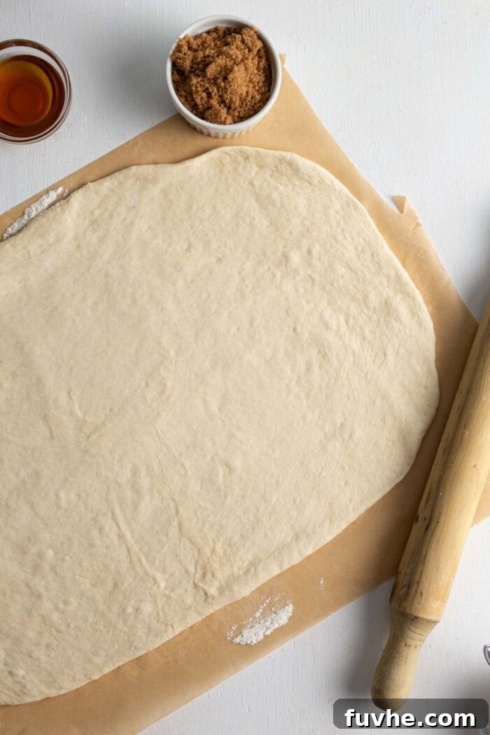 Large rectangle of cinnamon roll dough, evenly rolled out on a piece of parchment paper, ready for filling.