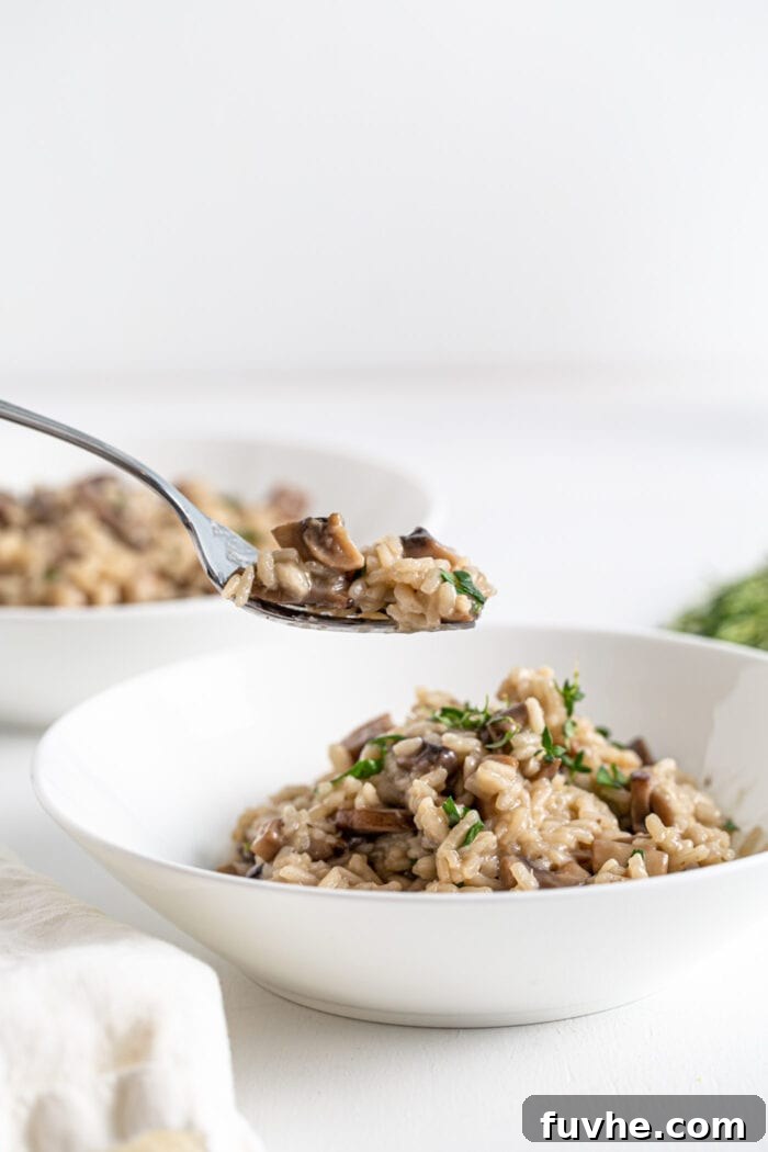 A spoon lifting a perfect spoonful of creamy vegan mushroom risotto out of a bowl, showcasing its rich texture and deliciousness.