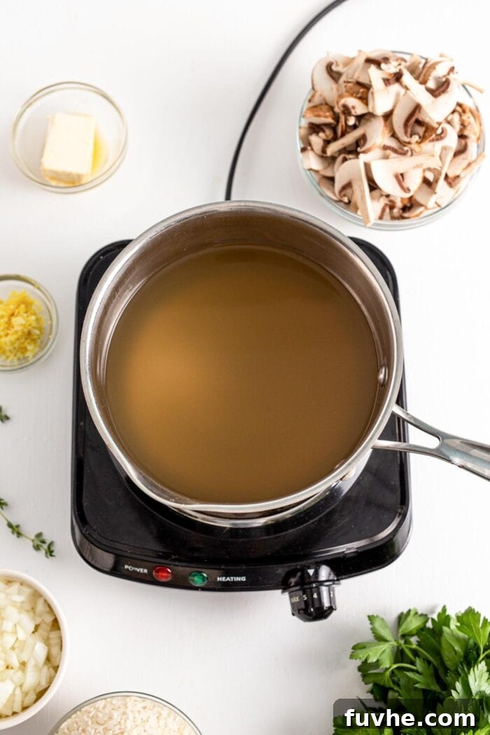 A large pot on a stovetop, filled with hot, simmering vegetable broth, with steam gently rising, indicating it's perfectly warmed for risotto.