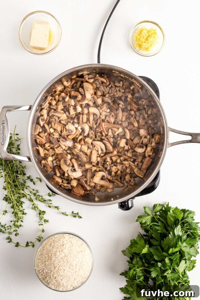 Finely chopped mushrooms cooking in a skillet on a cooktop, with steam visibly rising, indicating active cooking and moisture release.