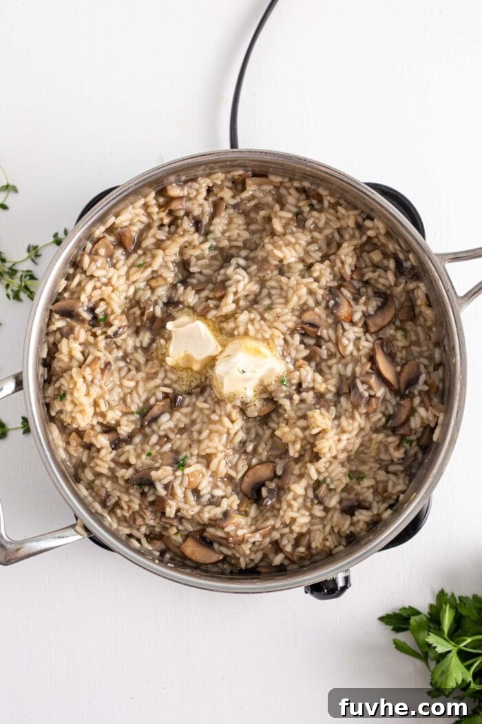 A large pot filled with creamy vegan mushroom risotto, topped with a pat of vegan butter and fresh parsley on the side, ready for finishing touches.