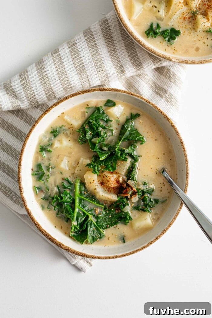 Creamy Plant Based Zuppa Toscana 9 A close-up, overhead view of a single bowl of rich, creamy Zuppa Toscana soup, featuring visible chunks of potato and bright green kale, with a spoon nestled in the inviting broth.