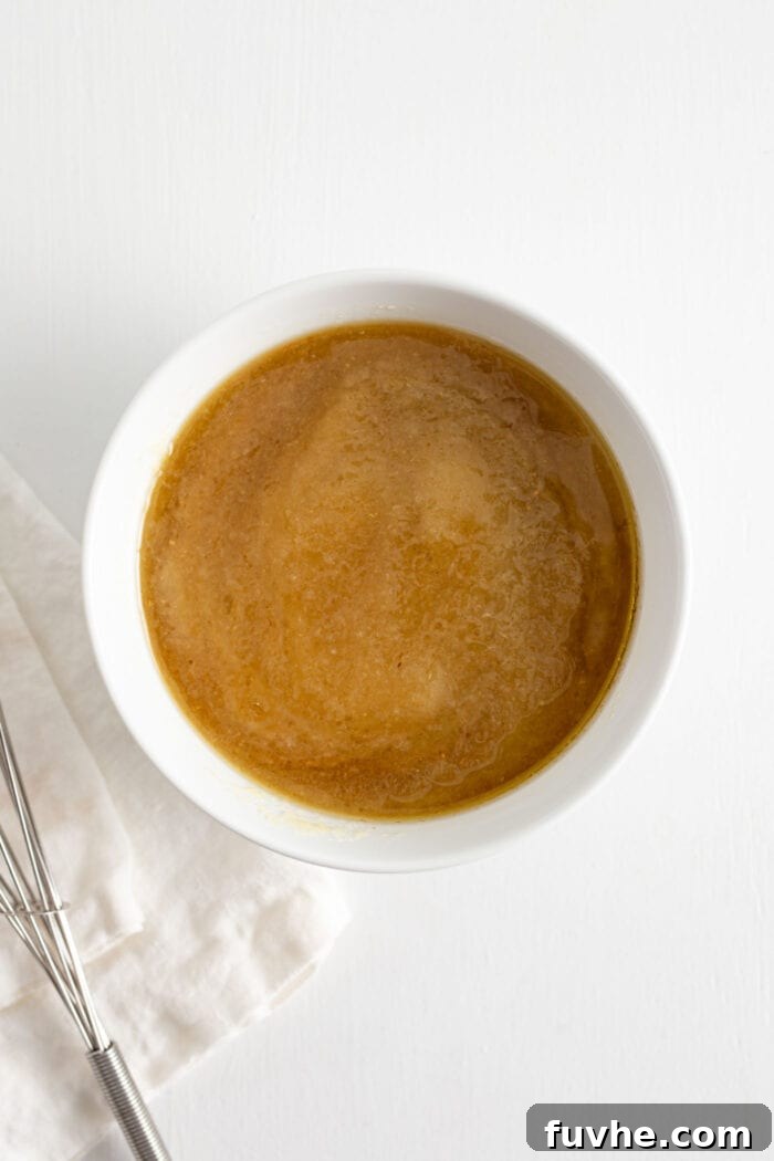 Applesauce, maple syrup and coconut oil mixed together in a glass mixing bowl.