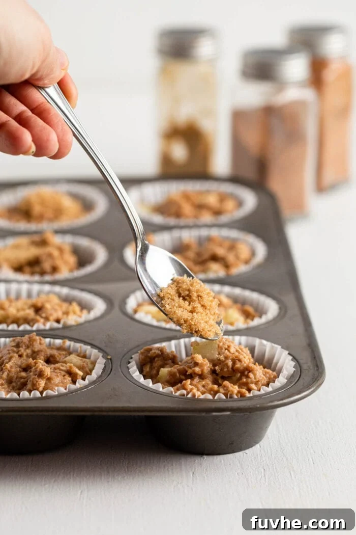 Spooning brown sugar onto a raw muffin in a muffin tin.