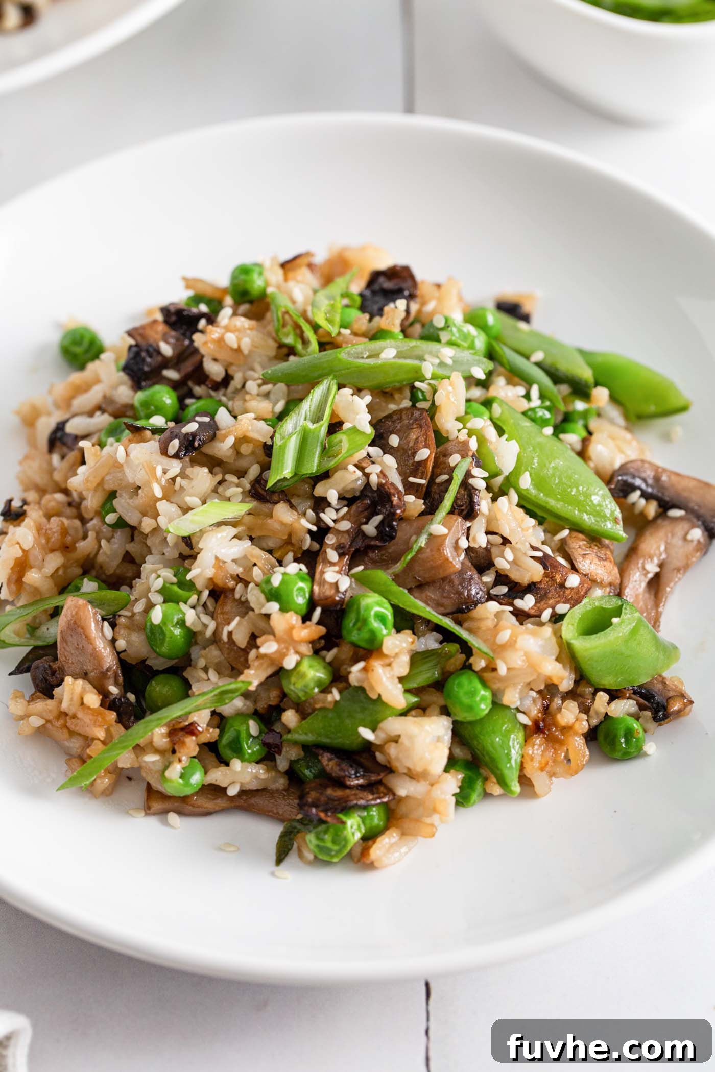 A beautifully plated dish of Chinese mushroom fried rice, garnished with toasted sesame seeds and fresh spring onions, ready to be enjoyed.