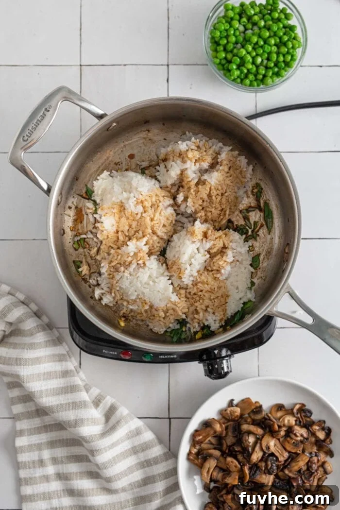 Perfectly cooked rice coated with savory soy sauce, being stir-fried in a skillet, absorbing all the delicious flavors.