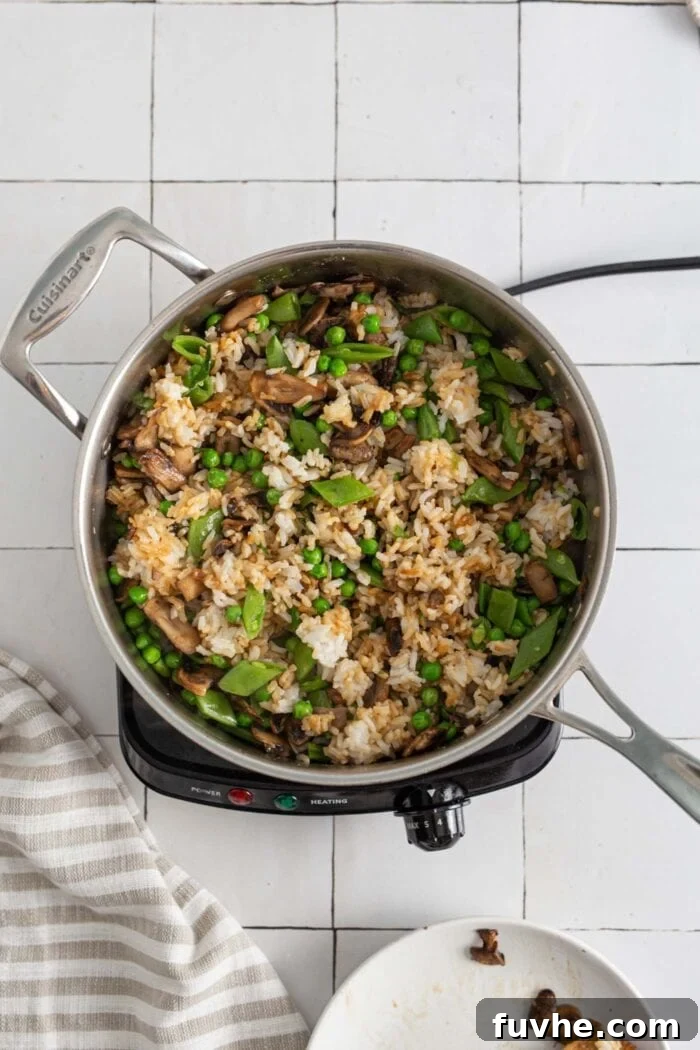 A vibrant mix of stir-fried mushrooms, snap peas, and green peas perfectly integrated into the fried rice within a large skillet.