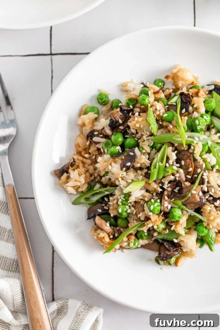 An inviting overhead shot of a plate of Chinese mushroom fried rice, beautifully garnished with bright spring onions and golden sesame seeds.
