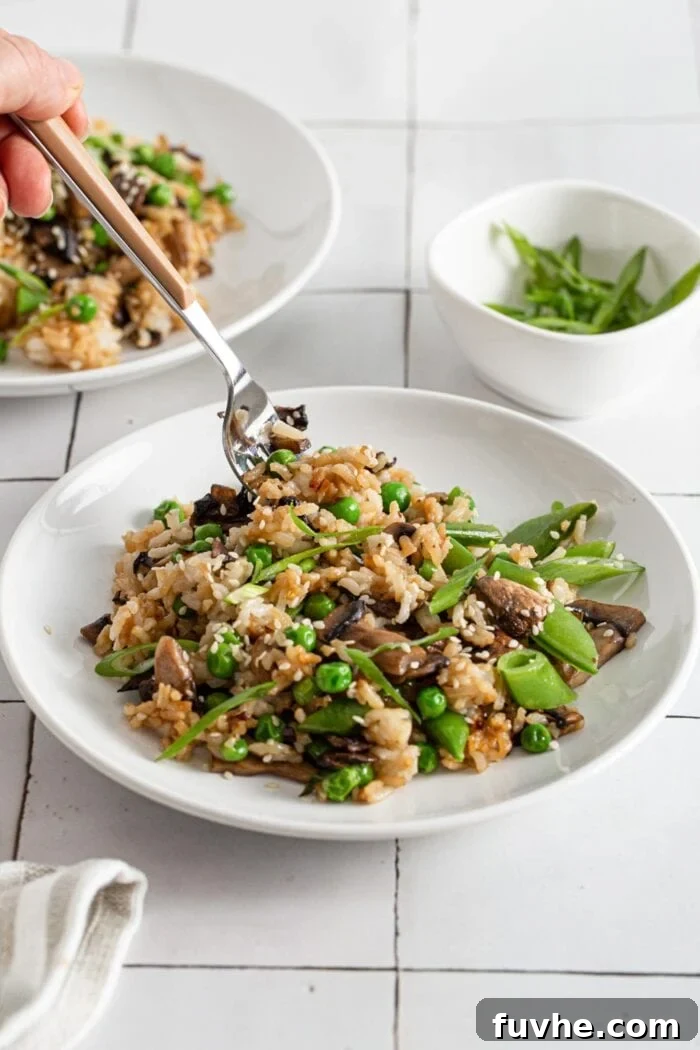 A hand holding a fork, poised to take a delicious forkful of the hot, savory vegan mushroom fried rice from a plate.