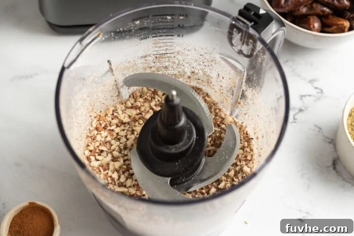 Raw almonds being blended into a grainy consistency inside a food processor bowl, ready for the next ingredients to be added for the no-bake bars.