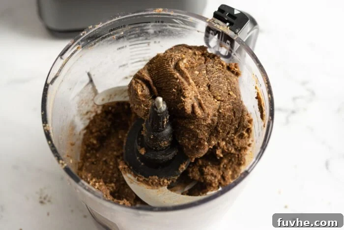 A thick, sticky dough mixture, made from dates, ground almonds, and hemp protein powder, formed inside a food processor, indicating it's ready for pressing into a pan.