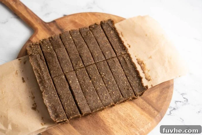 A large slab of no-bake hemp protein bar mixture, expertly cut into 16 uniform portions on a wooden cutting board, showcasing the final product before individual serving.