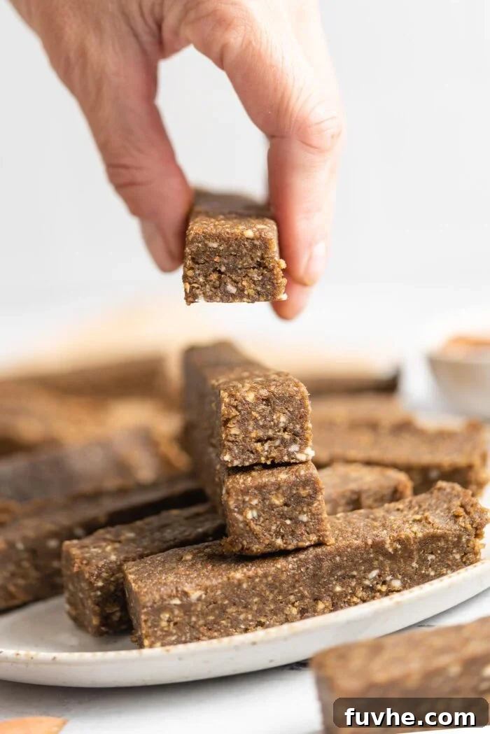 A hand reaching to pick up a single vegan hemp protein bar from a neatly stacked pile on a white plate, highlighting the bar's texture and inviting appeal.