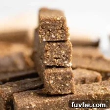 Stack of 3 no-bake almond hemp protein bars on a plate. More hemp bars are in the foreground and background, highlighting the ease of making homemade vegan protein bars.
