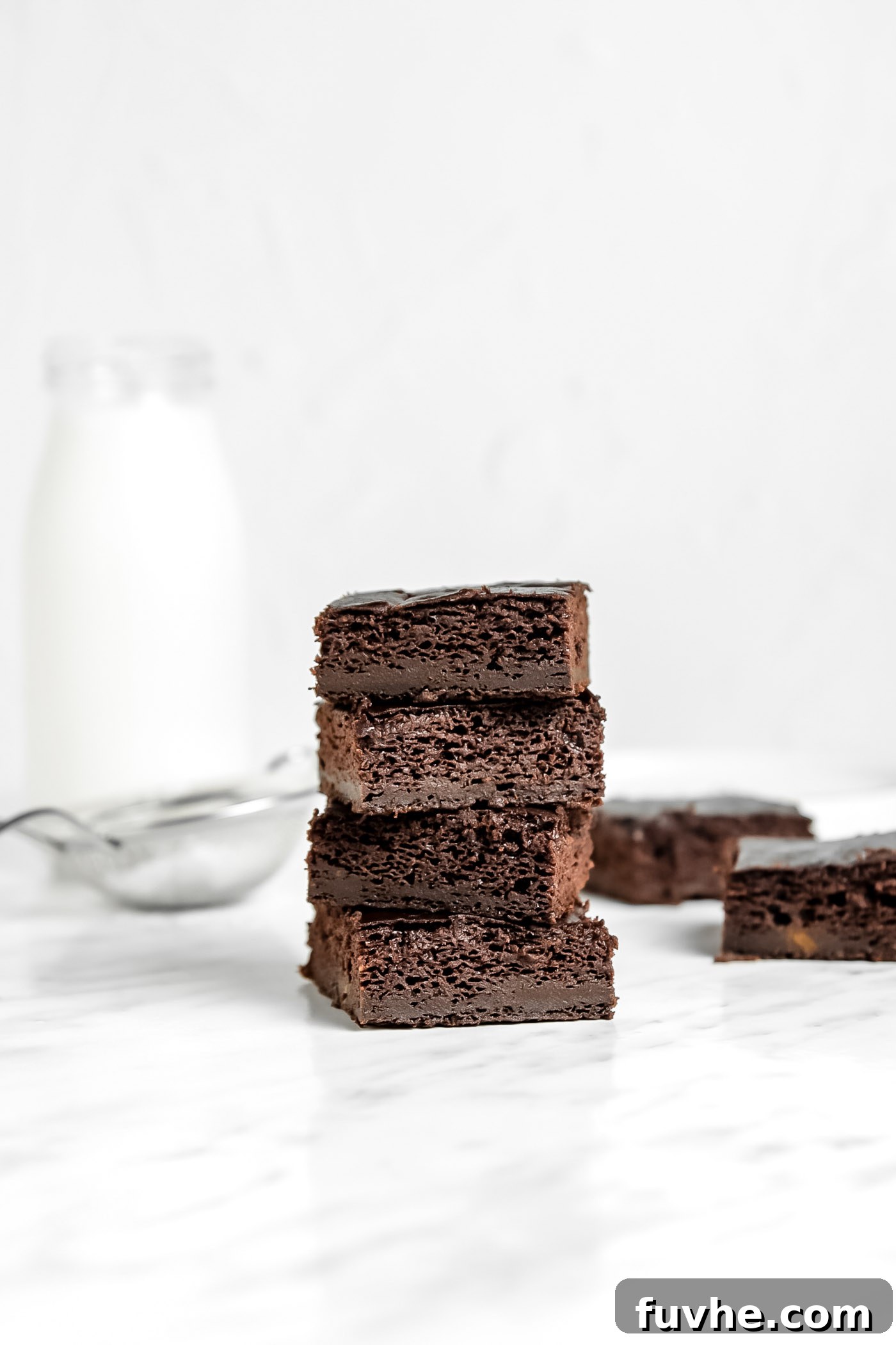 A stack of four fudgy vegan sweet potato brownies on a elegant marble surface, garnished with a sprinkle of cocoa.