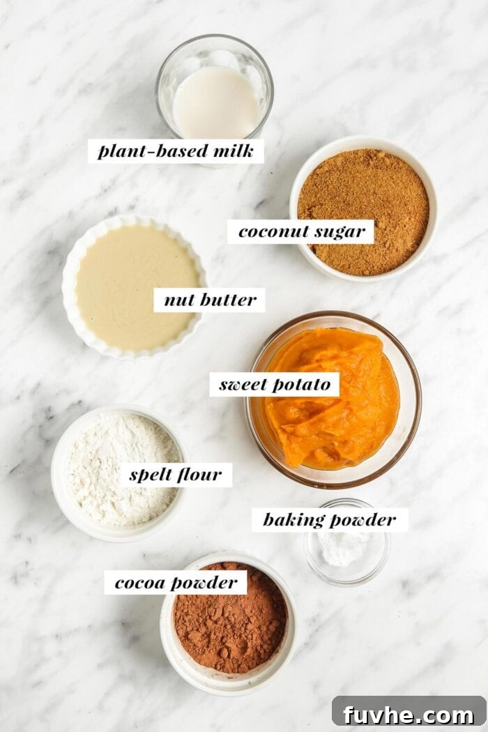 All the essential ingredients for making healthy sweet potato brownies laid out on a clean surface, including sweet potato, almond butter, cocoa, and flour.