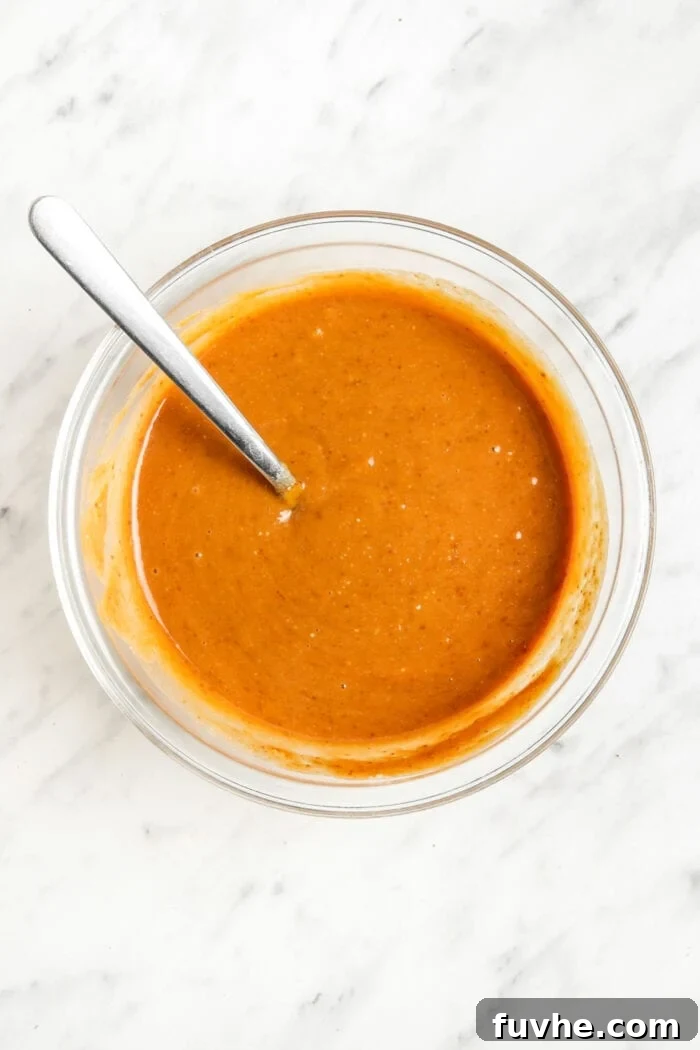 Raw sweet potato brownie batter, consisting of wet ingredients, perfectly mixed together in a large mixing bowl with a spoon.