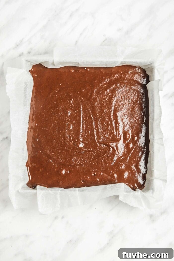 Raw sweet potato chocolate chip brownie batter spread evenly in a square baking tray lined with parchment paper, ready for baking.