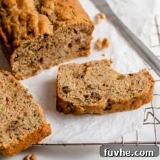 Sliced zucchini loaf resting on parchment paper on top of a cooling rack.
