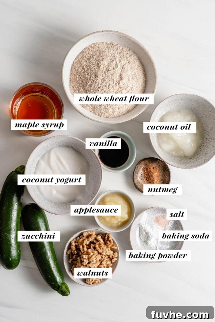 Wholesome Plant-Based Zucchini Bread 3 Visual of all ingredients needed for making a zucchini loaf labelled with text overlay: zucchini, flour, baking powder, baking soda, salt, nutmeg, coconut oil, maple syrup, applesauce, yogurt, vanilla, walnuts.