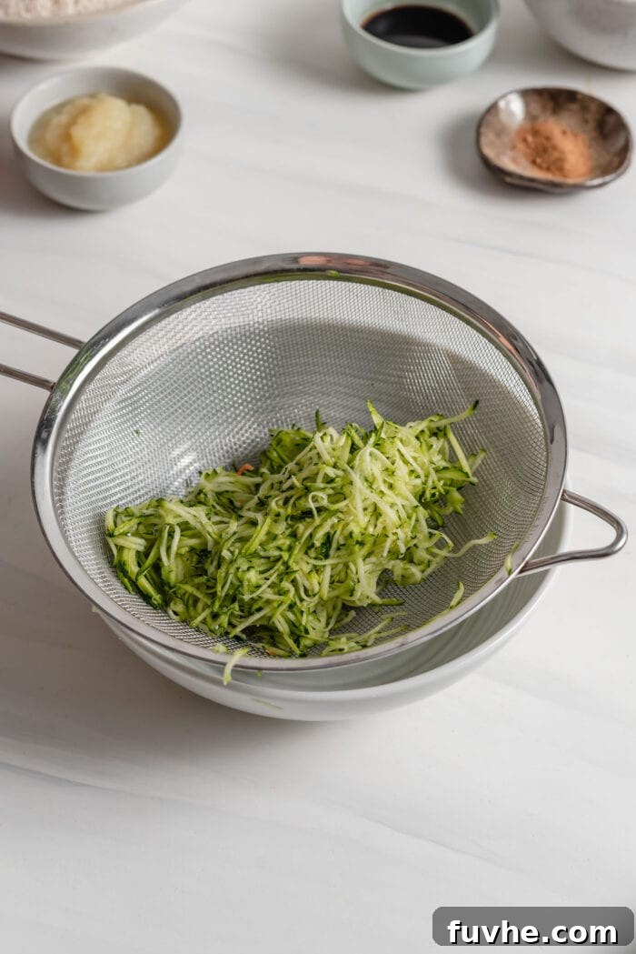 Wholesome Plant-Based Zucchini Bread 4 Grated zucchini in a strainer sitting in a bowl, showing the moisture being drained.