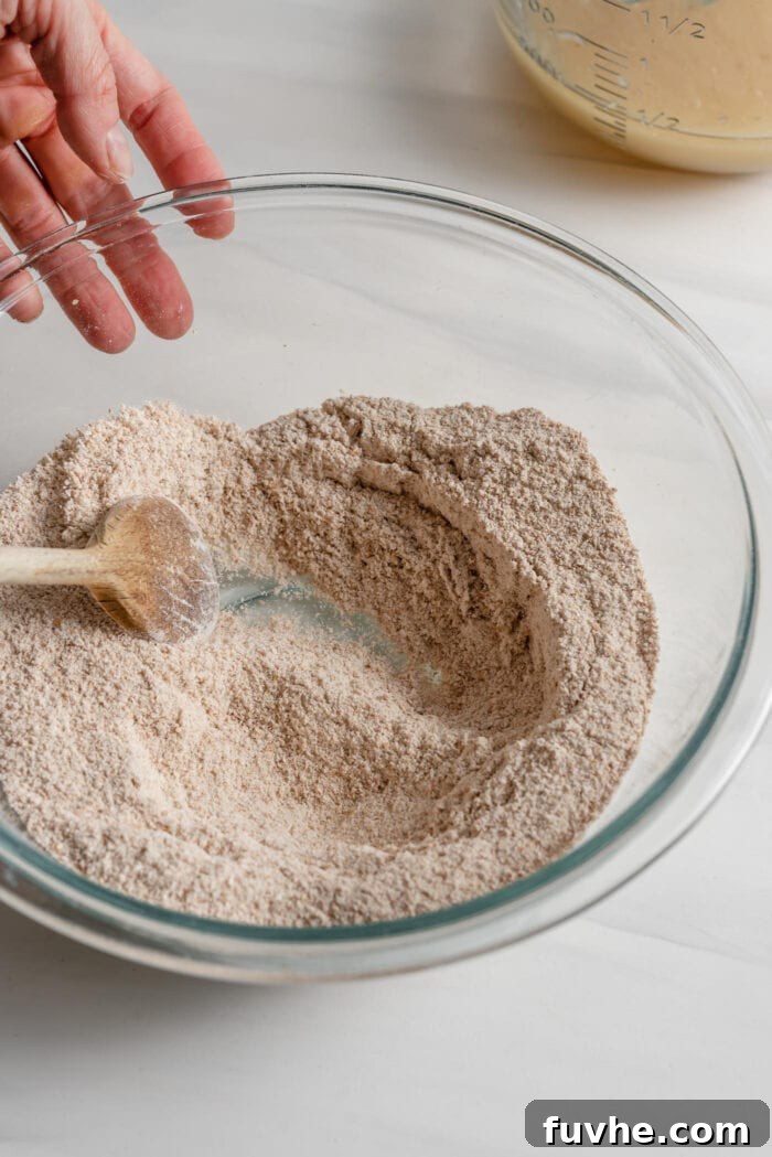 Wholesome Plant-Based Zucchini Bread 6 A wooden spoon mixing flour, baking powder, baking soda, nutmeg, and salt in a glass mixing bowl.