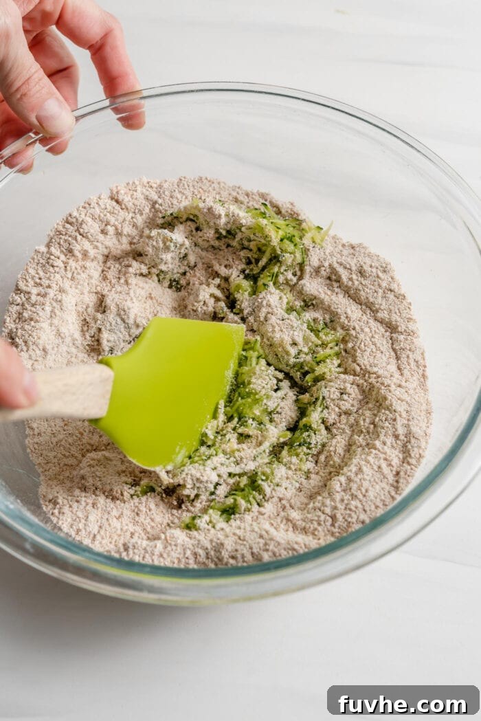 Wholesome Plant-Based Zucchini Bread 7 A spatula mixing grated zucchini into a bowl of dry flour mixture.