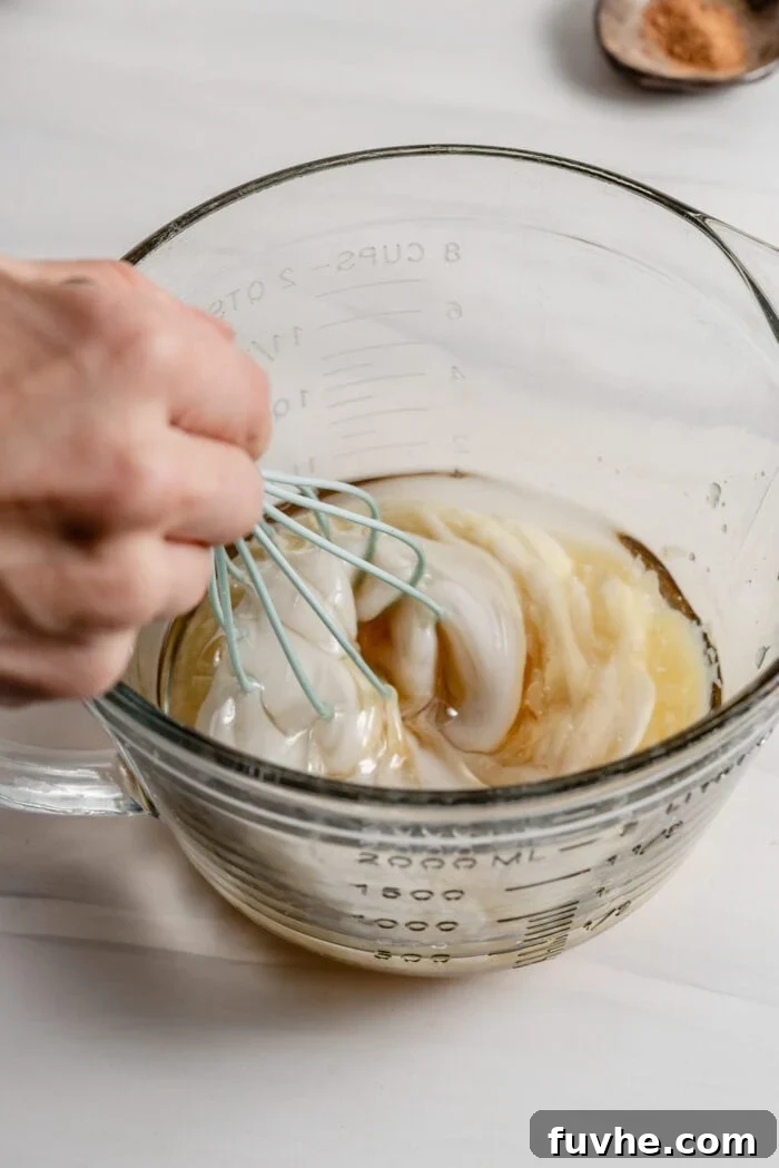 Wholesome Plant-Based Zucchini Bread 8 A whisk combining melted coconut oil and dairy-free yogurt in a glass mixing bowl.