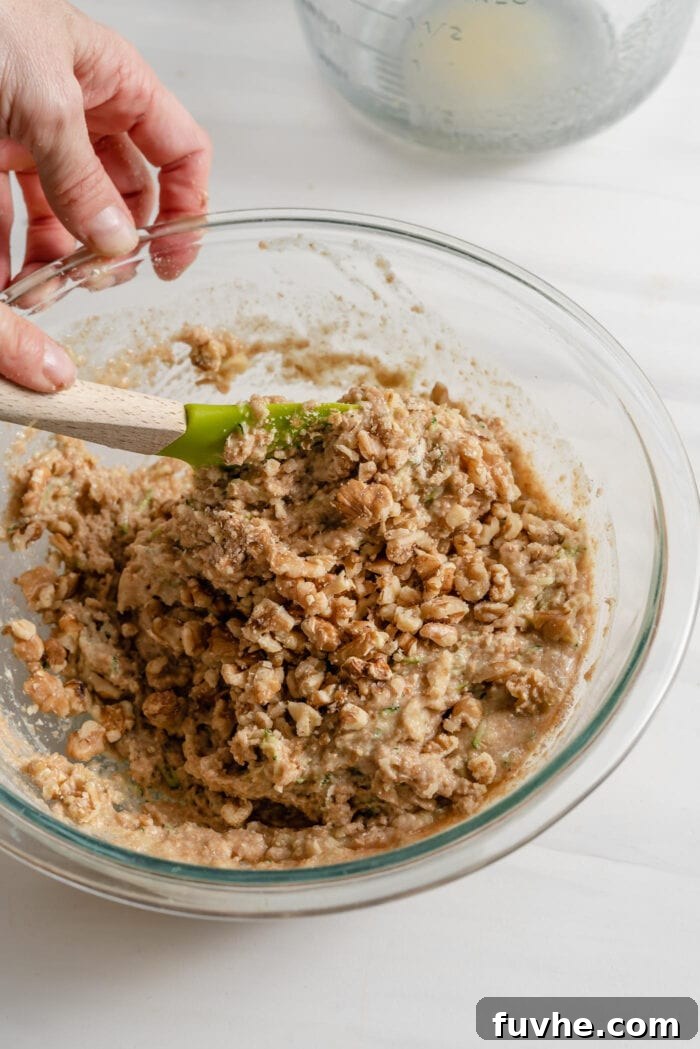 Wholesome Plant-Based Zucchini Bread 10 Folding chopped walnuts into raw zucchini bread batter in a large mixing bowl.