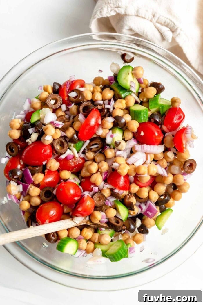 Chopped tomato, cucumber, olives, onion and chickpeas in a glass mixing bowl.