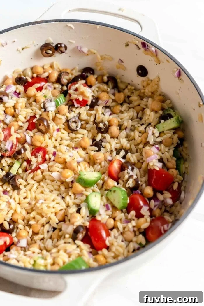 Mixed Mediterranean-style orzo salad with chickpeas and vegetables in a large pot.