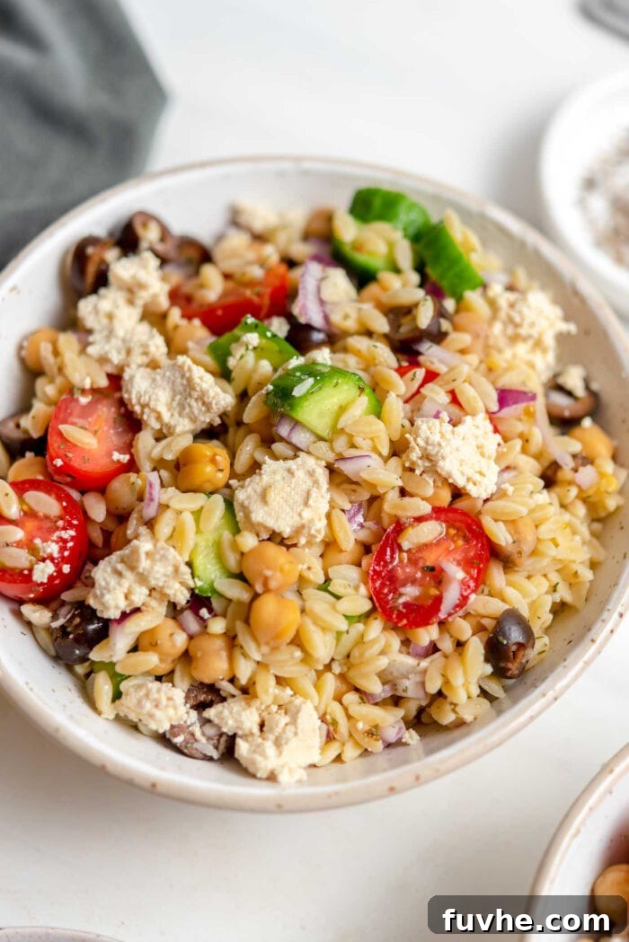 Close up of a bowl of Mediterranean orzo salad with tomato, cucumber and olives.